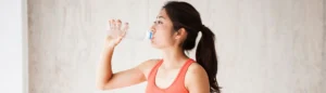 Une femme qui boit de l'eau (hydratation) en tenue de sport.