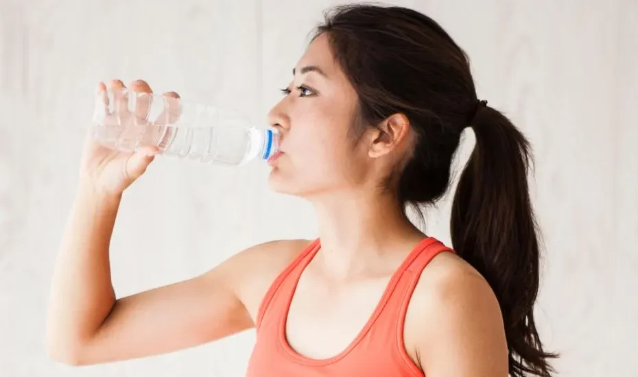 Une femme qui boit de l'eau (hydratation) en tenue de sport.
