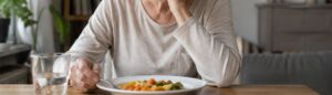 Une personne âgée qui ne mange plus, elle regarde son assiette pleine sans appétit.