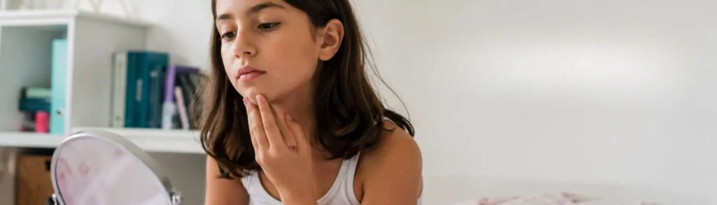 Une jeune fille atteinte de puberté précoce se regarde dans un miroir.