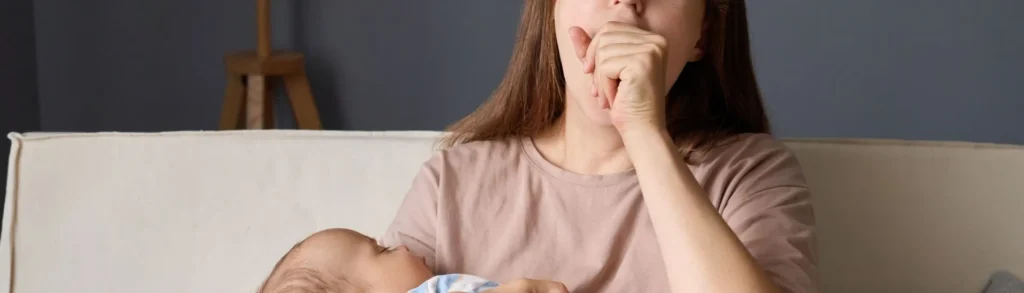 Une jeune maman baille proie à la fatigue avec son bébé dans les bras.