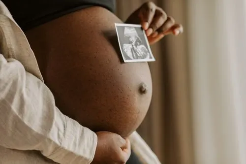 Une femme enceinte pose une photo de son échographie sur son ventre rond.