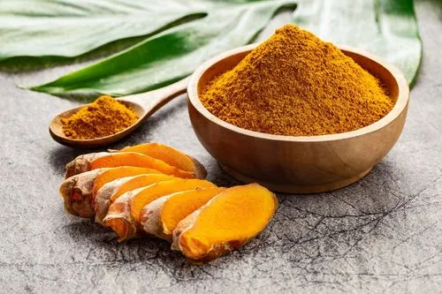 Photo de racines de curcuma à côté de poudre de curcuma.