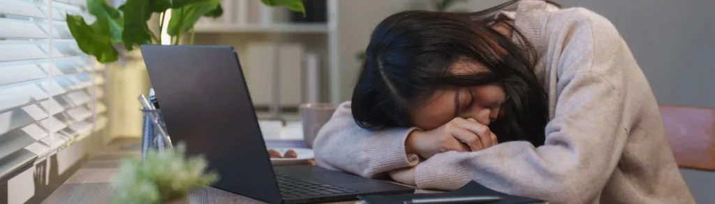 Une jeune femme assommée par la fatigue, qui dort sur son ordinateur.
