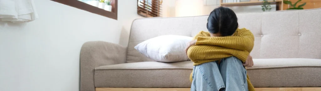 Une jeune femme dépressive assise par terre la tête entre les bras.